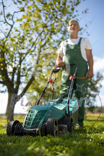 Senior gardenr gardening in his permaculture garden - mowing the lawn with an electrical lawn mower Senior gardenr gardening in his permaculture garden - mowing the lawn with an electrical lawn mower