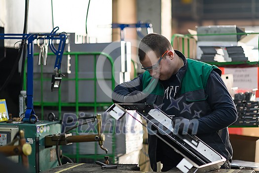 a uniformed worker working in a modern metal production and processing factory assembles parts of a new machine on his desk. High quality photo a uniformed worker working in a modern metal production and processing factory assembles parts of a new machine on his desk. High quality photo