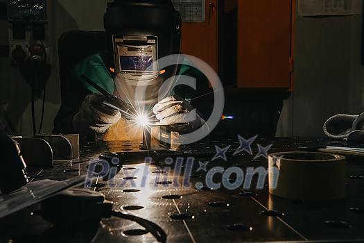A woman employed in a modern factory for the production and processing of metals in a work uniform welding metal materials. High quality photo A woman employed in a modern factory for the production and processing of metals in a work uniform welding metal materials. High quality photo