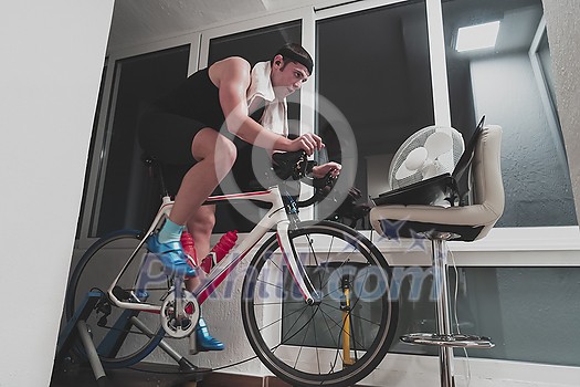 Man cycling on the machine trainer he is exercising in the home at night. Playing online bike racing game during coronavirus covid19 lockdown. New normal concept.