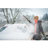 Pretty, young woman cleaning her car from snow after heavy snowstorm (color toned image)
