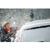 Pretty, young woman cleaning her car from snow after heavy snowstorm (color toned image)