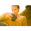 Hobby photographer concept. Outdoor lifestyle portrait of young woman taking photos with her mirrorless camera in warm evening sunlight