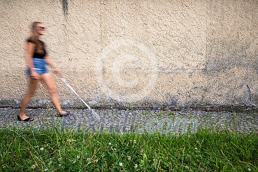 Blind woman walking on city streets, using her white cane to navigate the urban space better and to get to her destination safely Blind woman walking on city streets, using her white cane to navigate the urban space better and to get to her destination safely