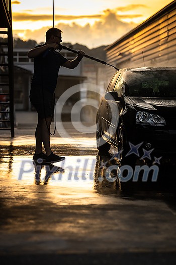 Young man washing his beloved car carefully in a manual car wash to prevent any damage and detail it properly Young man washing his beloved car carefully in a manual car wash to prevent any damage and detail it properly