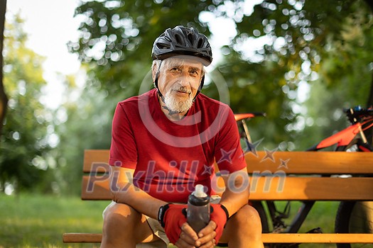 Senior man with his mountain bike going for a ride past the city limits in a lovely forest, getting the daily cardio dose, having a break on a bench Senior man with his mountain bike going for a ride past the city limits in a lovely forest, getting the daily cardio dose, having a break on a bench