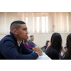 student taking notes while studying in high school. Satisfied young man looking at camera while sitting at desk in classroom. Portrait of college guy writing while completing assignment.