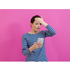 a disappointed-faced girl looks at her cell phone as she stands in front of a pink background
