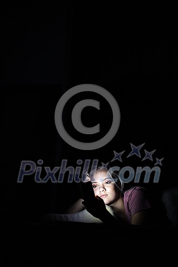 Teenage girl using her cell phone in a dark bedroom at night Teenage girl using her cell phone in a dark bedroom at night