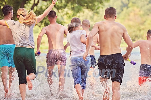 Summer joy group of happy friends having fun while running and splashing on river Summer joy group of happy friends having fun while running and splashing on river
