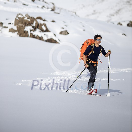 Winter sports - young man walking with snowshoes in high mountains covered with lots of snow (selective focus on the mountain in the background) Winter sports - young man walking with snowshoes in high mountains covered with lots of snow (selective focus on the mountain in the background)