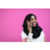 a beautiful afro girl smiling broadly uses a cell phone in front of a pink background
