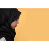 Modern African Muslim woman makes traditional prayer to God, keeps hands in praying gesture, wears traditional white clothes, has serious facial expression, isolated over plastic yellow background
