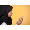 Modern African Muslim woman makes traditional prayer to God, keeps hands in praying gesture, wears traditional white clothes, has serious facial expression, isolated over plastic yellow background
