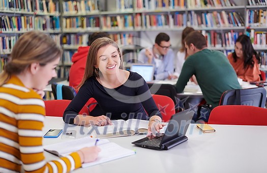 Two students taking notes from a book at library. Young two woman sitting at table doing assignments in college library. Two students taking notes from a book at library. Young two woman sitting at table doing assignments in college library.