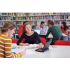 Two students taking notes from a book at library. Young two woman sitting at table doing assignments in college library.