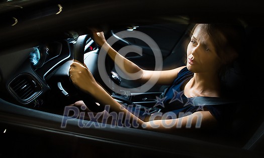 Driving a car at night - pretty, young woman driving her modern car at night, in a city (shallow DOF; color toned image) Driving a car at night - pretty, young woman driving her modern car at night, in a city (shallow DOF; color toned image)