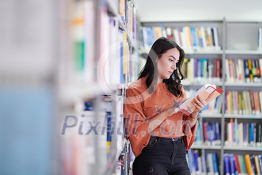 Reading a book in library. Young attractive librarian reading a book between library bookshelves Reading a book in library. Young attractive librarian reading a book between library bookshelves