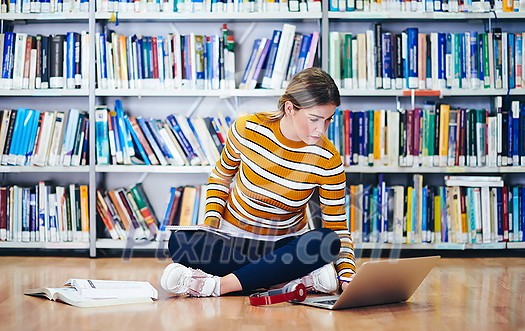 Woman student taking notes from a book at library. Young woman sitting and doing assignments in college library. Woman student taking notes from a book at library. Young woman sitting and doing assignments in college library.