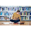 Woman student taking notes from a book at library. Young woman sitting and doing assignments in college library.