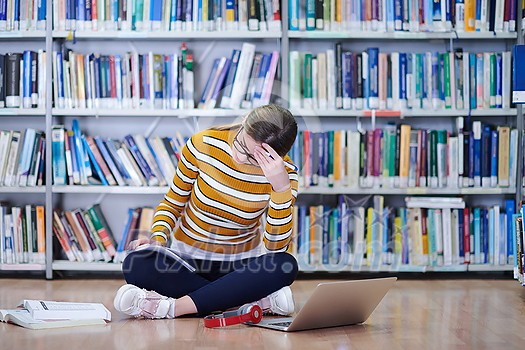 Woman student taking notes from a book at library. Young woman sitting and doing assignments in college library. Woman student taking notes from a book at library. Young woman sitting and doing assignments in college library.