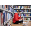 a young student with glasses sits in the library, reads a book and makes notes with a latpop