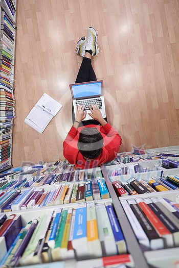 top view of a young student with glasses sits in the library, reads a book and makes notes with a latpop top view of a young student with glasses sits in the library, reads a book and makes notes with a latpop
