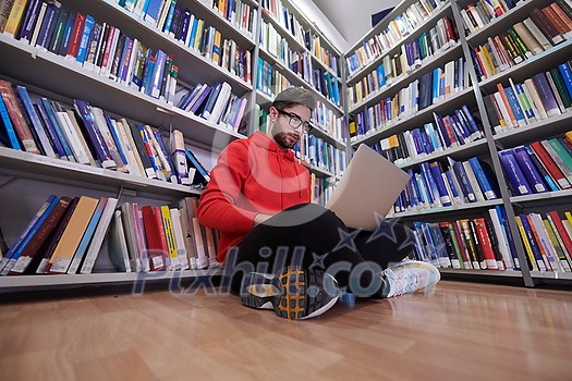 a young student with glasses sits in the library, reads a book and makes notes with a latpop a young student with glasses sits in the library, reads a book and makes notes with a latpop