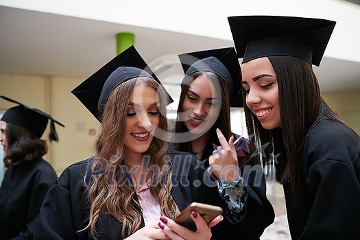 education, graduation, technology and people concept - group of happy international students in mortar boards and bachelor gowns with diplomas using martphone education, graduation, technology and people concept - group of happy international students in mortar boards and bachelor gowns with diplomas using martphone