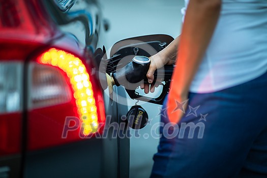Young female driver refueling her car at night with gas(color toned image; shallow DOF) Young female driver refueling her car at night with gas(color toned image; shallow DOF)