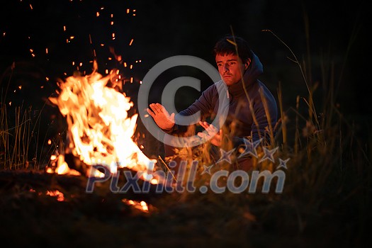 Young man making fire while camping outdoors, in an alpine wilderness - warming up his hands Young man making fire while camping outdoors, in an alpine wilderness - warming up his hands
