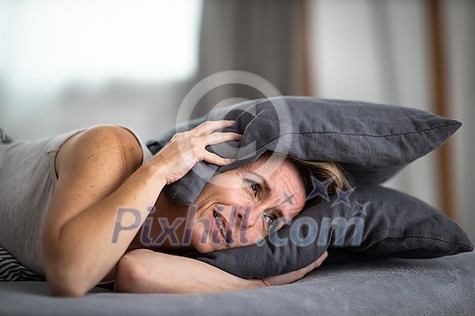 Sleepless lady covering ears with pillow. Noisy neighbors, tinnitus, insomnia or stress concept. Tired woman can't sleep. Awake in bed after coming home from her shift, work. Sleepless lady covering ears with pillow. Noisy neighbors, tinnitus, insomnia or stress concept. Tired woman can't sleep. Awake in bed after coming home from her shift, work.