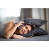 Sleepless lady covering ears with pillow. Noisy neighbors, tinnitus, insomnia or stress concept. Tired woman can't sleep. Awake in bed after coming home from her shift, work.