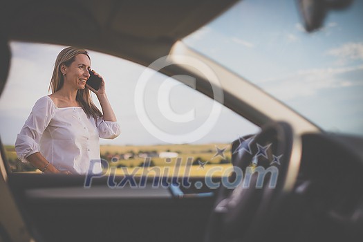Pretty midle aged woman at the steering wheel of her car, having a break on a long trip, making a phone call Pretty midle aged woman at the steering wheel of her car, having a break on a long trip, making a phone call