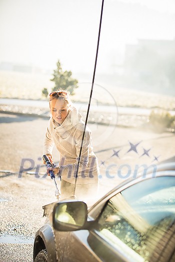 Pretty, young woman washing her car in a manual carwash (color toned image) Pretty, young woman washing her car in a manual carwash (color toned image)