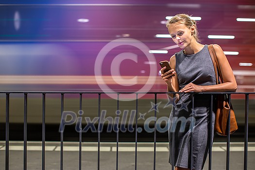 Pretty, young female commuter waiting for her daily train in a modern trainstation, using her cellphone while waiting (color toned image) Pretty, young female commuter waiting for her daily train in a modern trainstation, using her cellphone while waiting (color toned image)