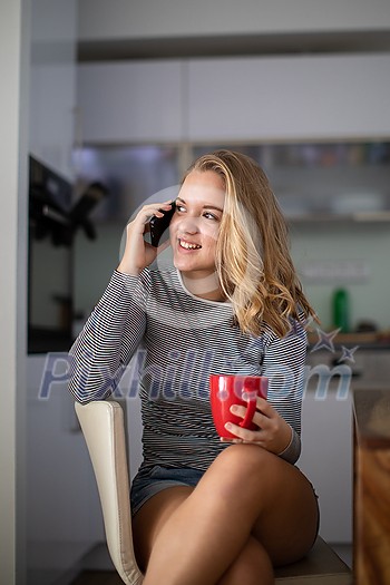 Teenage girl calling on her cell phone while having a cup of tea in modern kitchen setting (shalllow DOF, color toned image) Teenage girl calling on her cell phone while having a cup of tea in modern kitchen setting (shalllow DOF, color toned image)