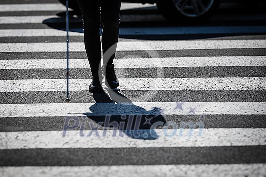 Blind woman walking on city streets, using her white cane to navigate the urban space better and to get to her destination safely Blind woman walking on city streets, using her white cane to navigate the urban space better and to get to her destination safely