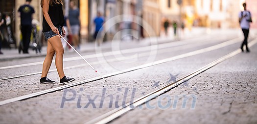 Blind woman walking on city streets, using her white cane to navigate the urban space better and to get to her destination safely Blind woman walking on city streets, using her white cane to navigate the urban space better and to get to her destination safely