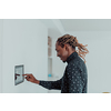 Smiling African American man using modern smart home system, controller on wall, positive young man switching temperature on thermostat or activating security alarm in apartment. High quality photo
