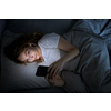 Young woman in bed holding a phone, tired and exhausted, blue light straining her eyes, messing up her circadian rhytm