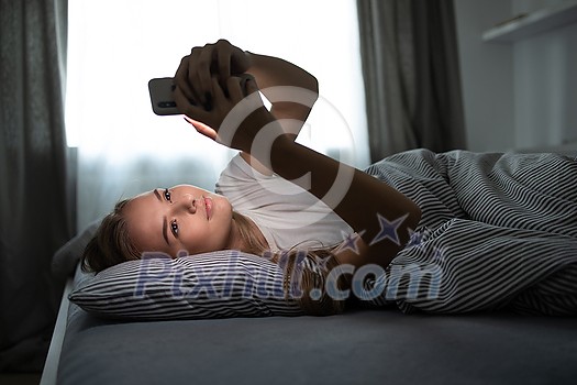 Pretty, young woman sleeping in her bed with her cell phone close to her. Smartphone in Bed Mobile/smartphone Addiction Concept. Pretty, young woman sleeping in her bed with her cell phone close to her. Smartphone in Bed Mobile/smartphone Addiction Concept.