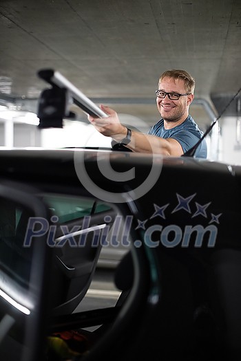 Handsome young driver getting ready to go biking - putting a bike rack on the roof of his car Handsome young driver getting ready to go biking - putting a bike rack on the roof of his car