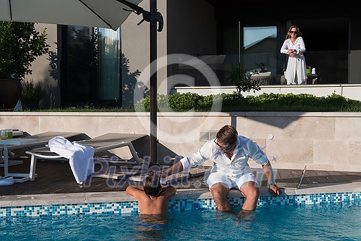 The happy family enjoys vacation in a luxury house with a pool. The senior couple spends time with their son during the vacation. Selective focus. High-quality photo The happy family enjoys vacation in a luxury house with a pool. The senior couple spends time with their son during the vacation. Selective focus. High-quality photo