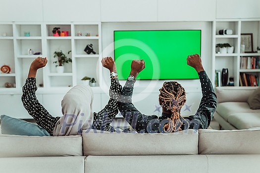 African Couple Sitting On Sofa Watching TV Together Chroma Green Screen Woman Wearing Islamic Hijab Clothes. High quality photo African Couple Sitting On Sofa Watching TV Together Chroma Green Screen Woman Wearing Islamic Hijab Clothes. High quality photo