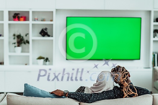 African Couple Sitting On Sofa Watching TV Together Chroma Green Screen Woman Wearing Islamic Hijab Clothes. High quality photo African Couple Sitting On Sofa Watching TV Together Chroma Green Screen Woman Wearing Islamic Hijab Clothes. High quality photo