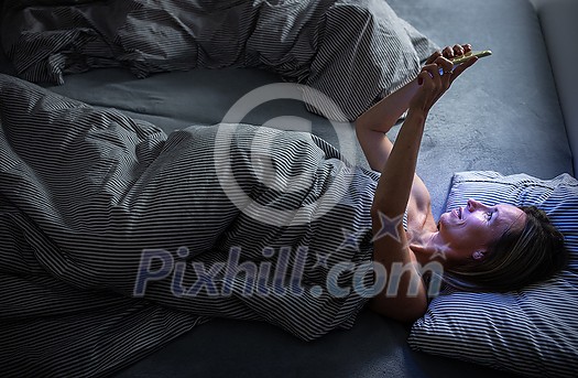 Middle-aged woman using her tablet computer before sleep in bed in the evening - exposure to blue light right before sleep Middle-aged woman using her tablet computer before sleep in bed in the evening - exposure to blue light right before sleep