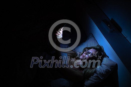 Pretty, middle-aged woman using her cell phone in bed at night - unhealthy blue light exposure Pretty, middle-aged woman using her cell phone in bed at night - unhealthy blue light exposure