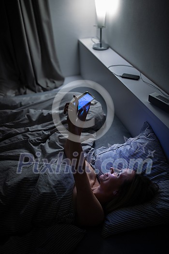 Middle-aged woman using her tablet computer before sleep in bed in the evening - exposure to blue light right before sleep Middle-aged woman using her tablet computer before sleep in bed in the evening - exposure to blue light right before sleep