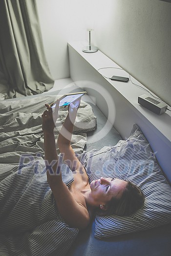 Middle-aged woman using her tablet computer before sleep in bed in the evening - exposure to blue light right before sleep Middle-aged woman using her tablet computer before sleep in bed in the evening - exposure to blue light right before sleep